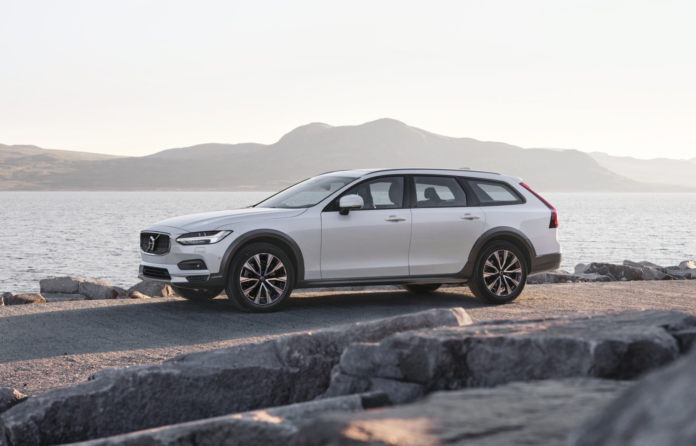 Volvo S90 INSCRIPTION in Mussel Blue metallic fährt auf einer Brücke, die über einen Fluss führt, im Hintergrund eine Stadt - Frontseitenschuss